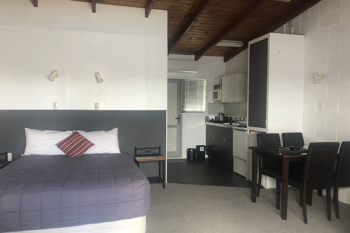 A hotel room with a bed, a desk, and a kitchenette.