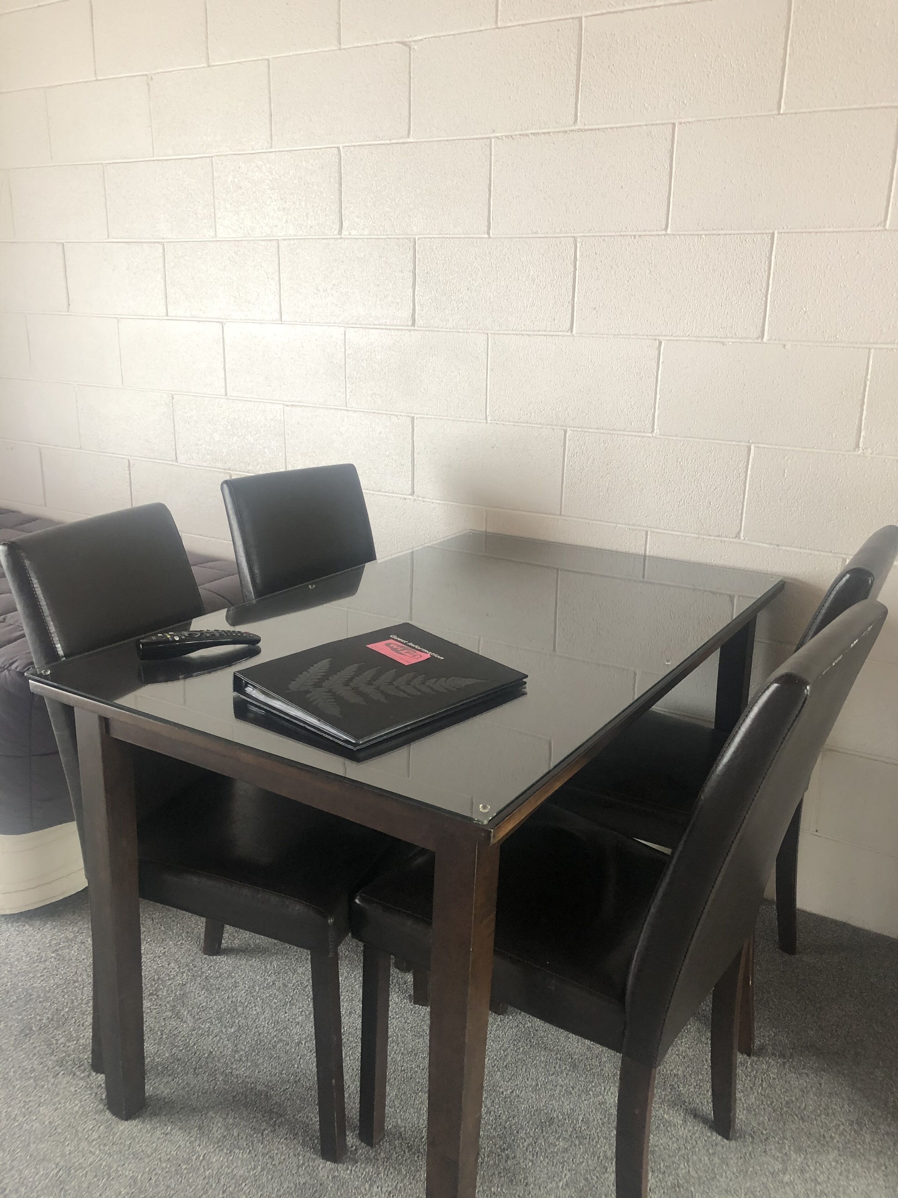 Una pequeña mesa de madera oscura con superficie de vidrio, rodeada por cuatro sillas de cuero negro. Sobre la mesa, una carpeta negra con etiqueta roja.