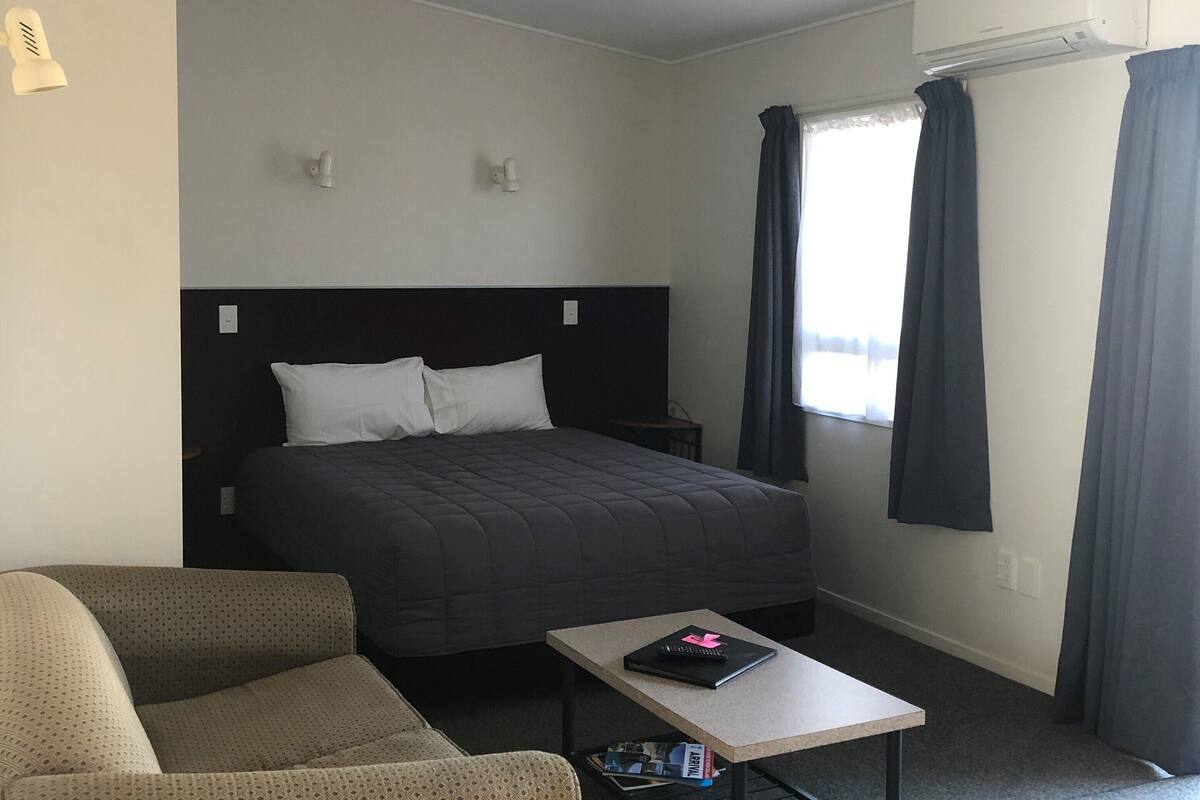 A hotel room with a bed, a sofa, a small table, and a ceiling fan.