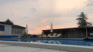 A swimming pool with lounge chairs and umbrellas, surrounded by buildings and trees. - Thornton Lodge Motel (Waipukurau)