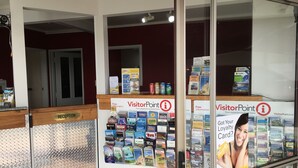 A reception area with a glass partition displaying travel brochures and a sign indicating free information. - Thornton Lodge Motel (Waipukurau)