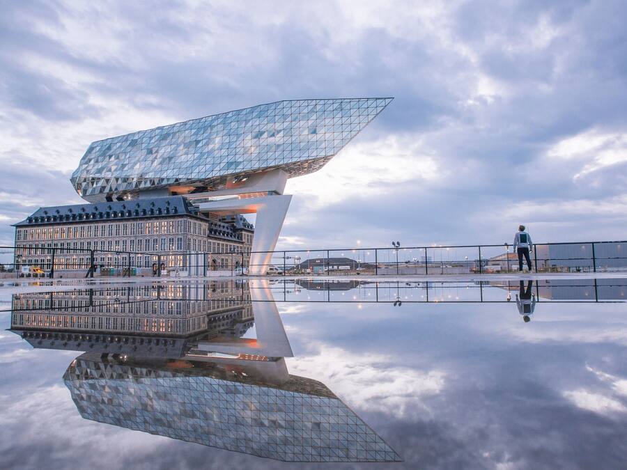 Un edifici modern amb un disseny geomètric únic, una gran façana de vidre i una superfície d'aigua reflectant al davant.