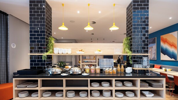 A modern kitchen area with a black and white tiled backsplash, wooden shelves with plates, and a central island with various kitchen items. - Holiday Inn Express Antwerp City Centre by IHG (Antwerp)