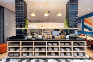 A modern kitchen area with a black and white tiled backsplash, wooden shelves with plates, and a central island with various kitchen items. - Holiday Inn Express Antwerp City Centre by IHG (Antwerp)