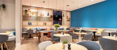 Un restaurante moderno con mesas redondas, sillas tapizadas en gris y una pared azul decorativa.