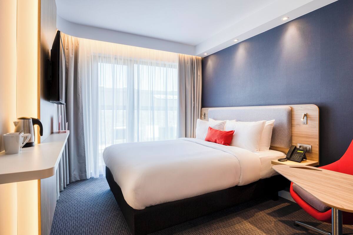 A modern hotel room with a large bed, a desk with a telephone, and a television mounted on the wall.
