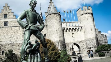 A statue of a knight in front of a castle with two towers and flags.