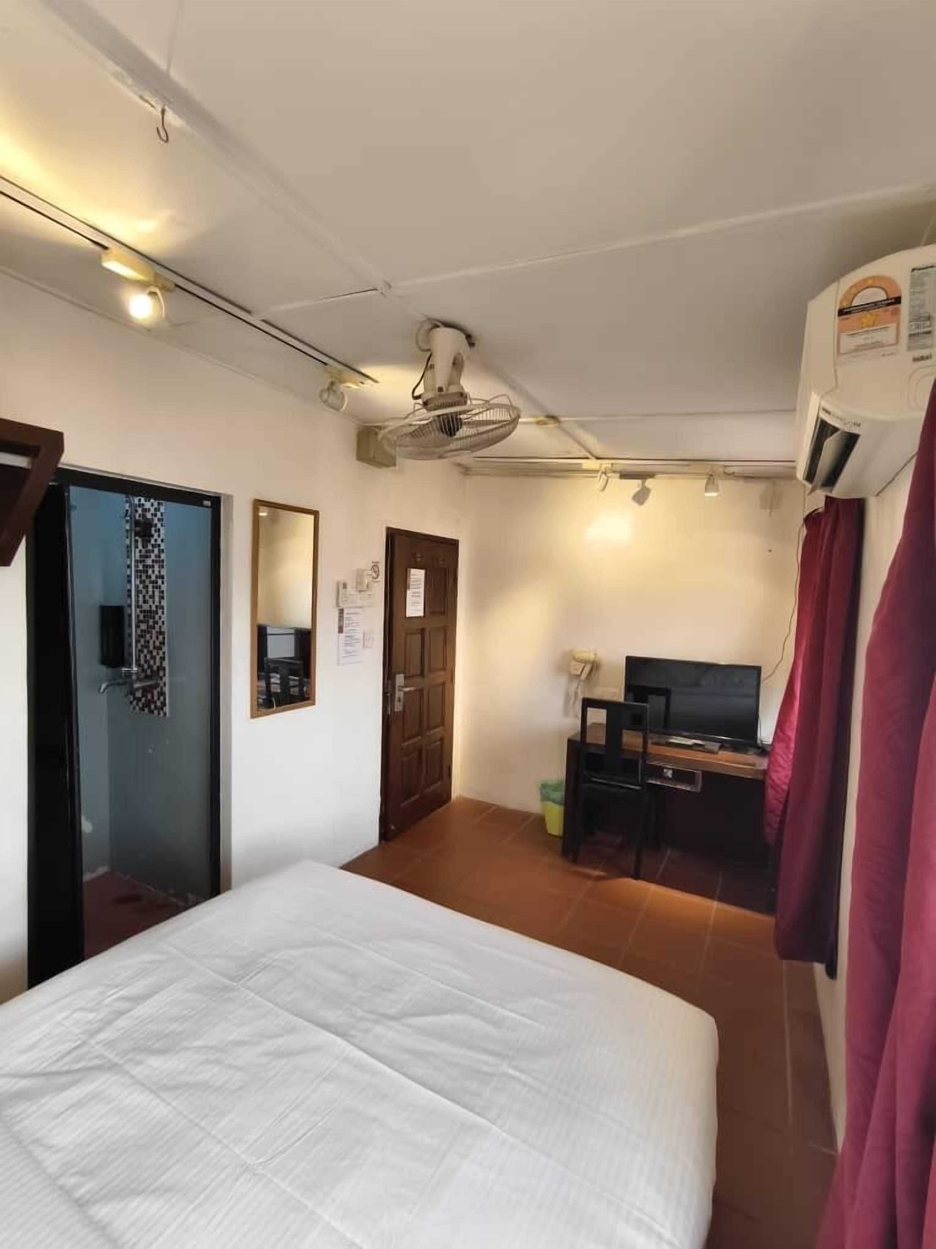 Une chambre d’hôtel comprenant un lit, un bureau avec un ordinateur, une télévision, un climatiseur et une porte avec un miroir.