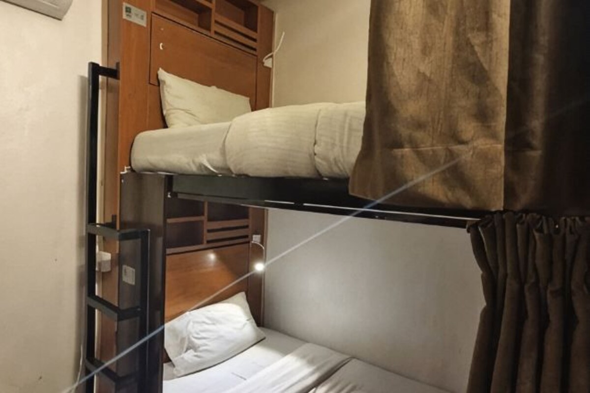 A bunk bed with a wooden headboard, a white pillow, and a brown curtain.