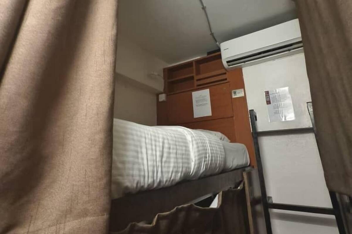 Un letto a castello con materasso e testiera, un condizionatore d'aria bianco e un armadietto in legno con una lavagna.