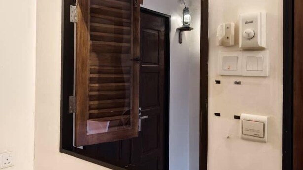 A room with a large mirror, a wooden door, and a wall-mounted light fixture.