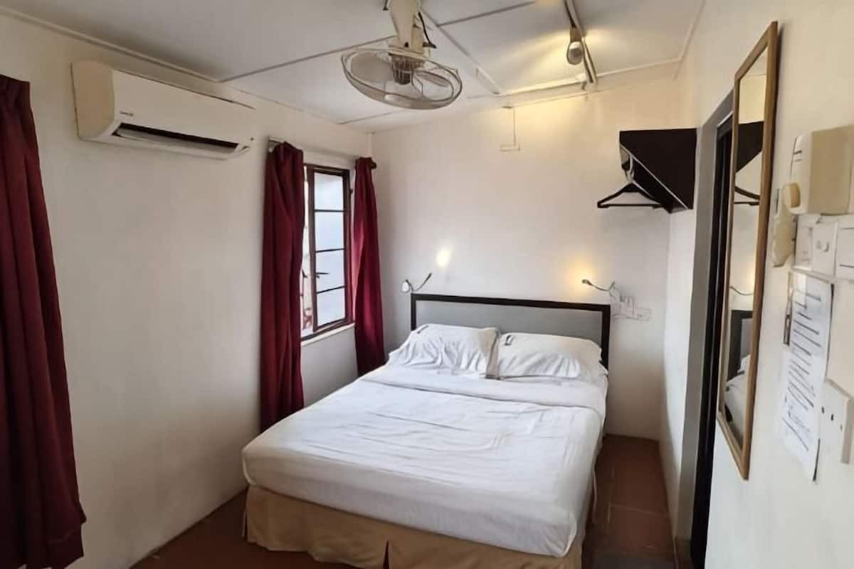 Una camera da letto con un letto, una finestra con tende, un condizionatore d'aria, una ventola a soffitto e un portalampada a parete.