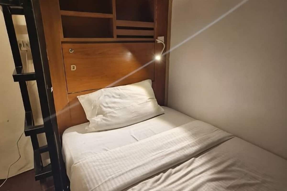 Un letto singolo con testiera in legno, una scala e una presa elettrica.