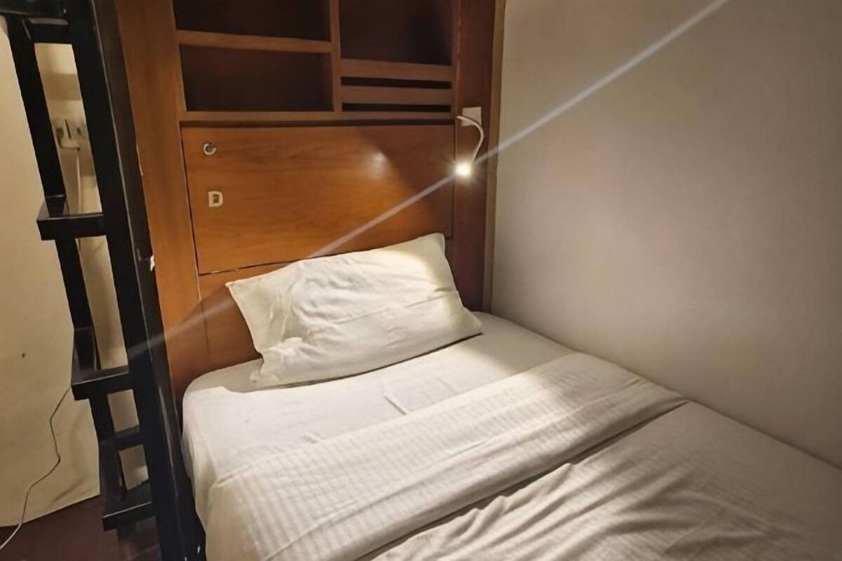 Un lit simple avec une tête de lit en bois, une échelle et une prise de courant au mur.