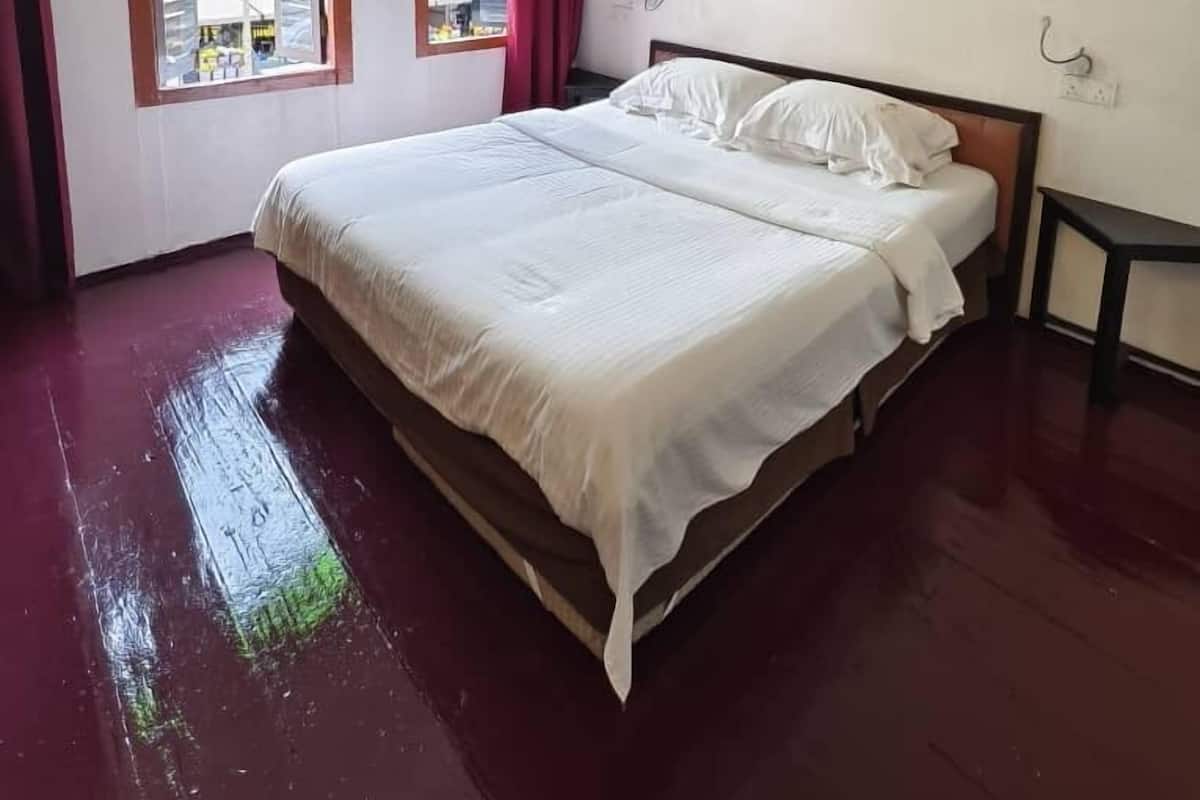 Una camera da letto con un letto, due finestre con tende, una ventola a soffitto e un quadro appeso al muro.
