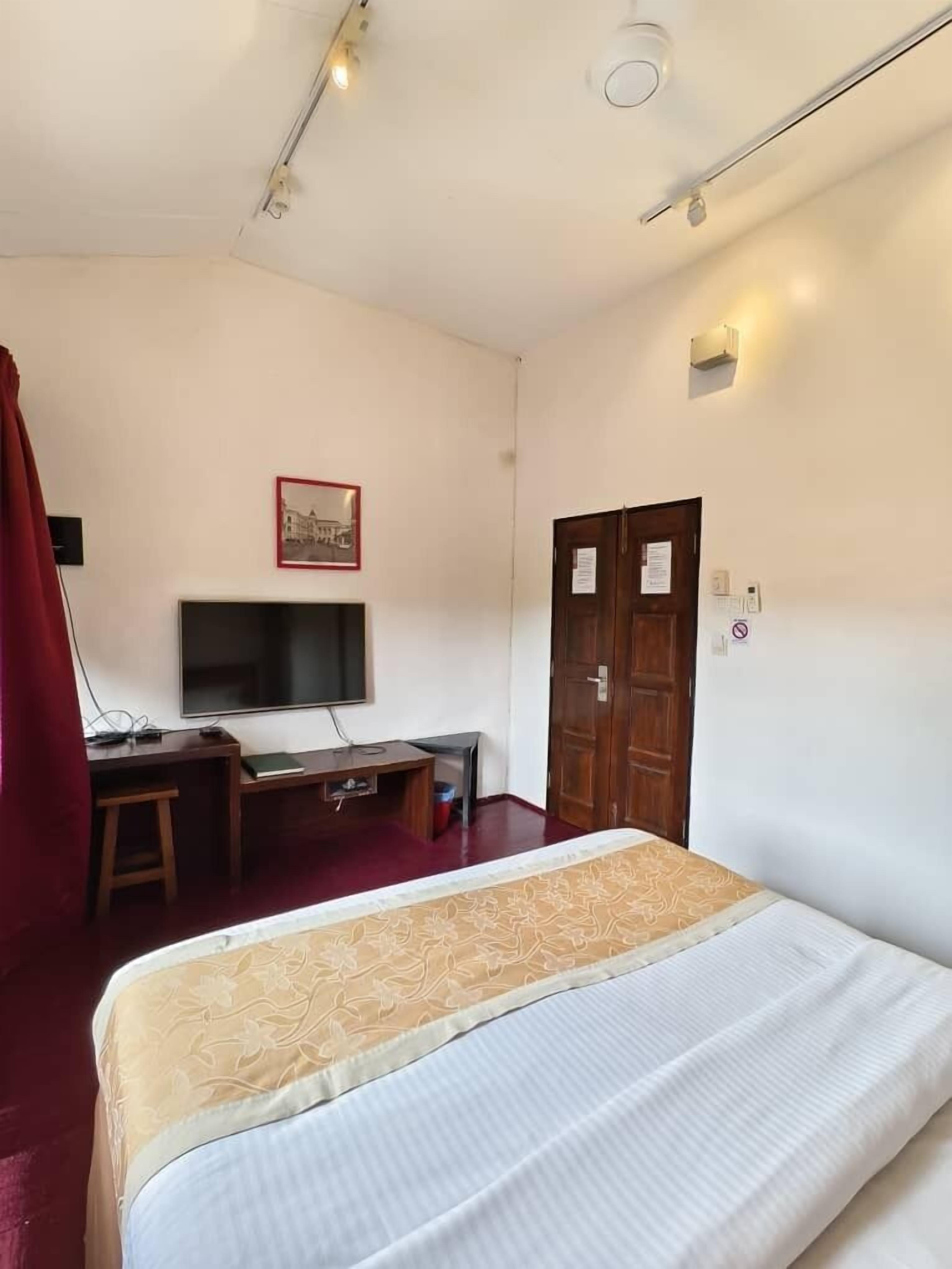 A hotel room with a bed, a desk with a computer, a television, and a door with a sign.