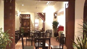 An indoor dining area with wooden tables and chairs, potted plants, and a staircase leading to another level.