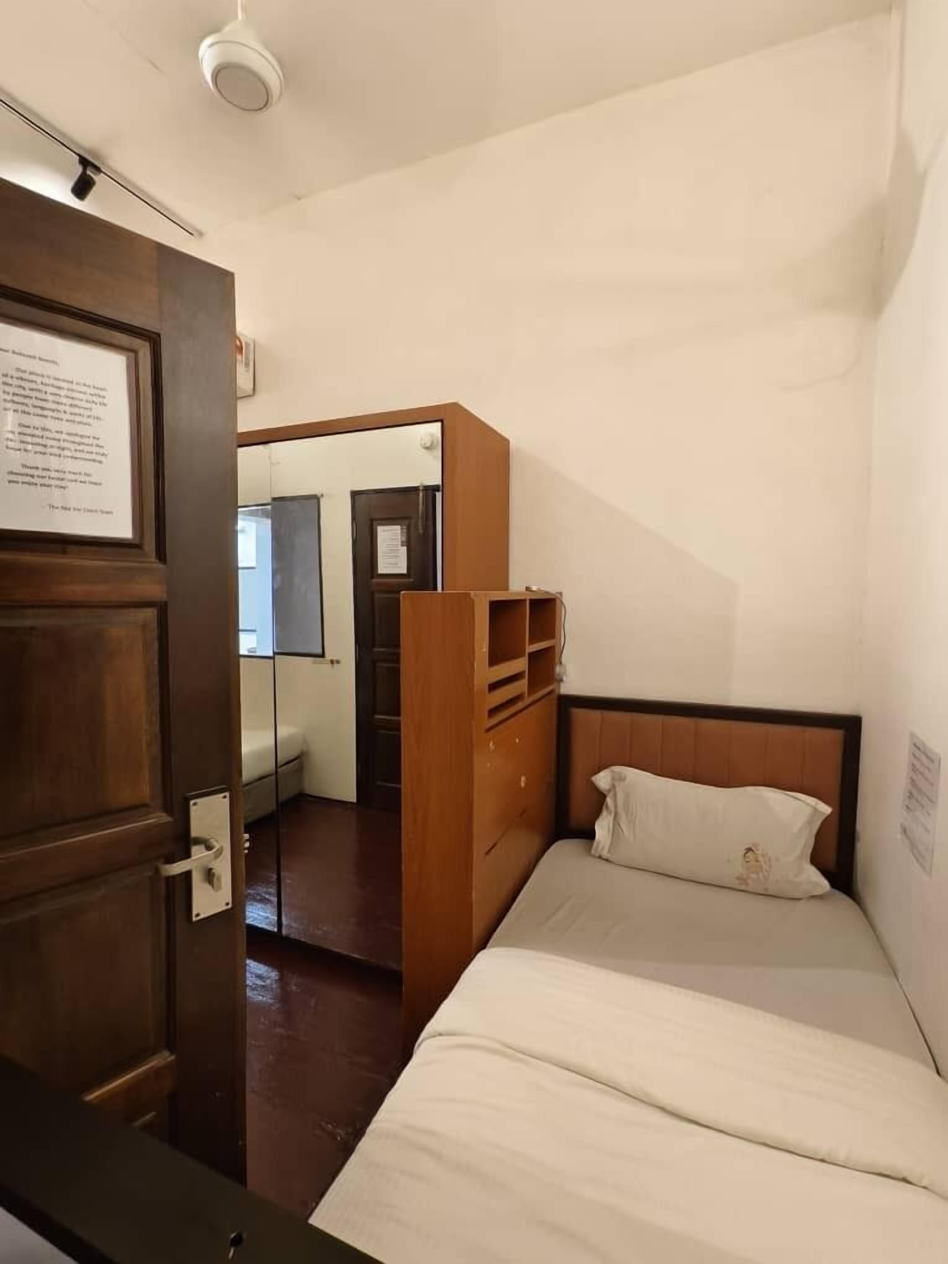 Un dormitorio pequeño y ordenado con una cama individual, un armario de madera y un espejo.