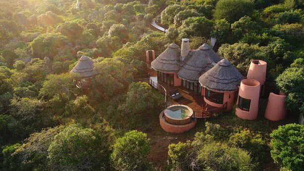 A secluded resort with thatched-roof villas, a central pool, and lush surrounding vegetation. - Thanda Safari (Hluhluwe)