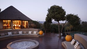 A spacious outdoor area with a curved seating arrangement, a fire pit, and a dining area with a thatched roof. - Thanda Safari (Hluhluwe)