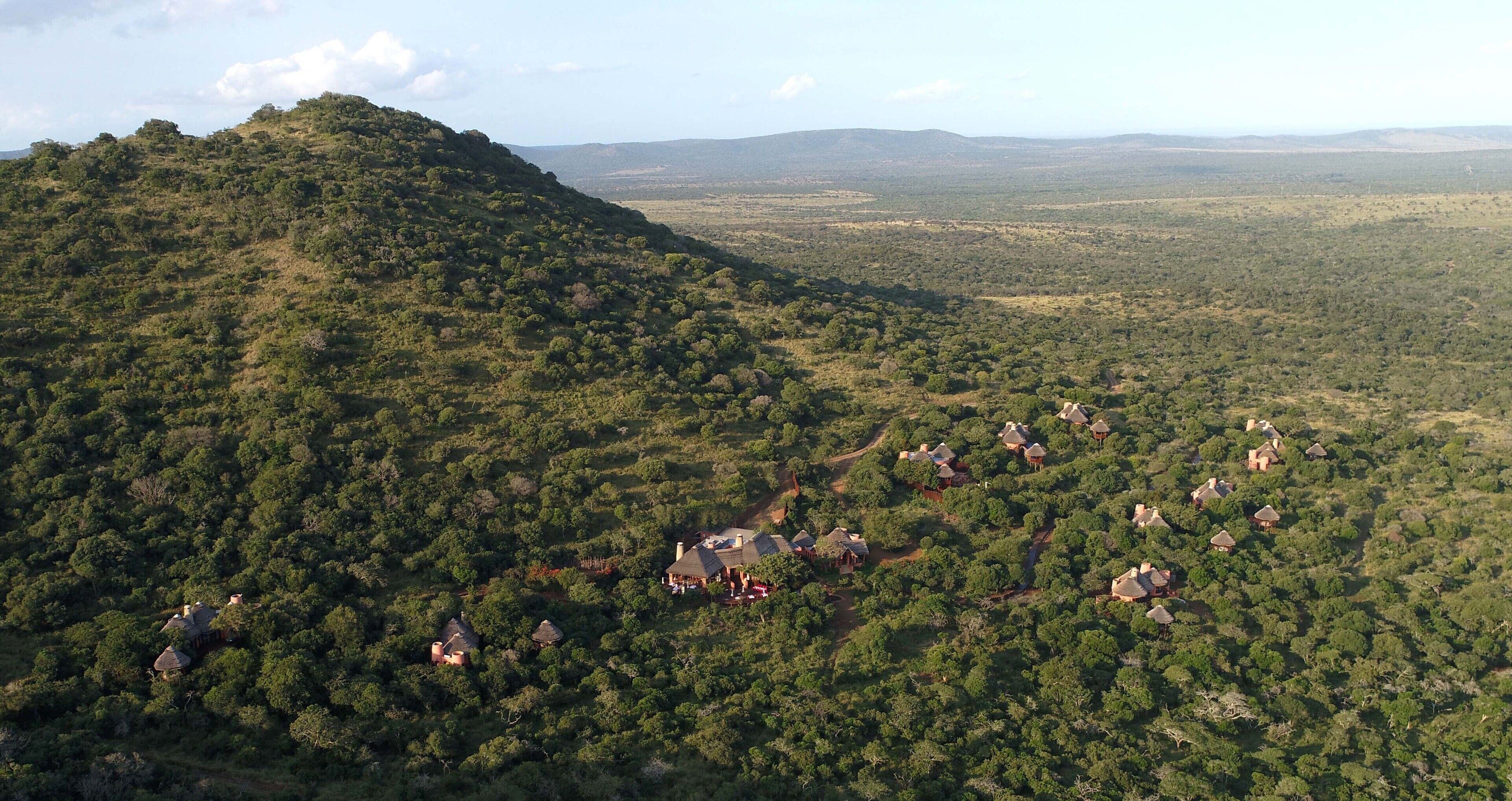 An aerial view of a hilly area with scattered buildings, likely a resort or lodge, surrounded by dense vegetation.