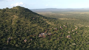 An aerial view of a hilly area with scattered buildings, likely a resort or lodge, surrounded by dense vegetation.