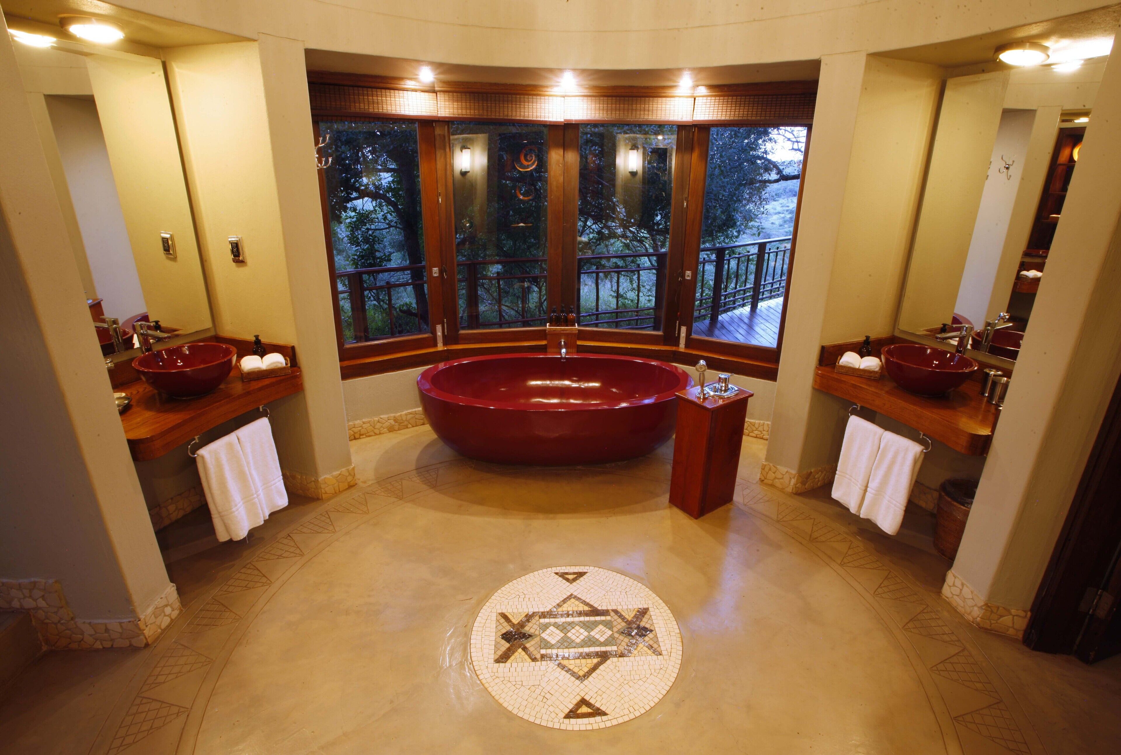 Un baño amplio con una bañera roja grande, dos lavamanos y un diseño de mosaico circular en el suelo.