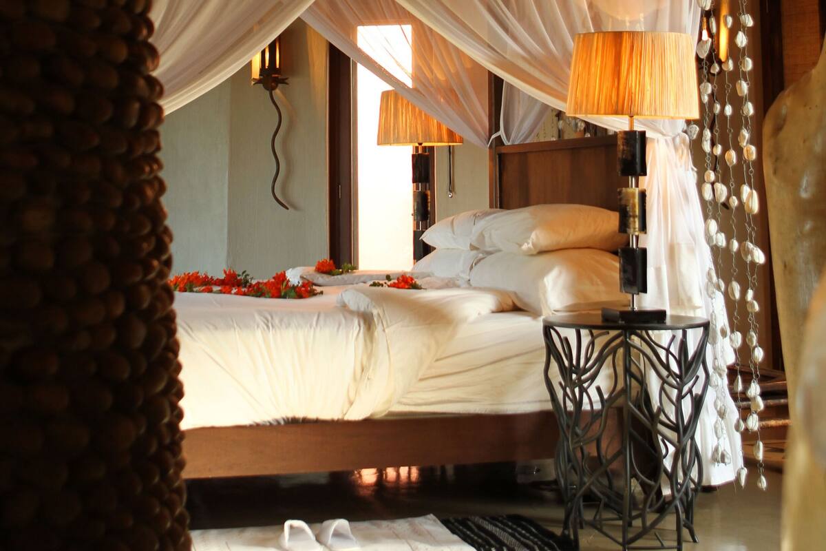A bedroom with a bed, bedside lamps, a wooden ceiling, and a decorative canopy.