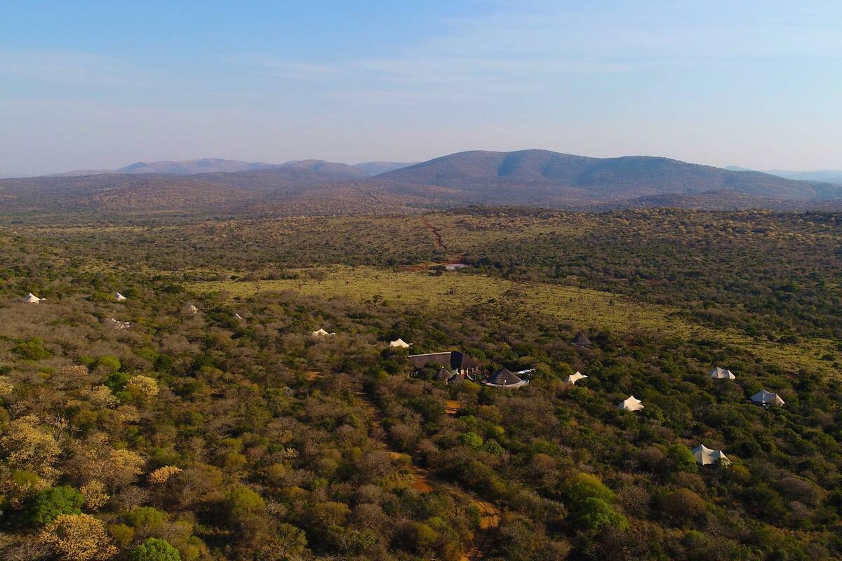 A rural landscape with scattered houses amidst dense vegetation and hills in the background.