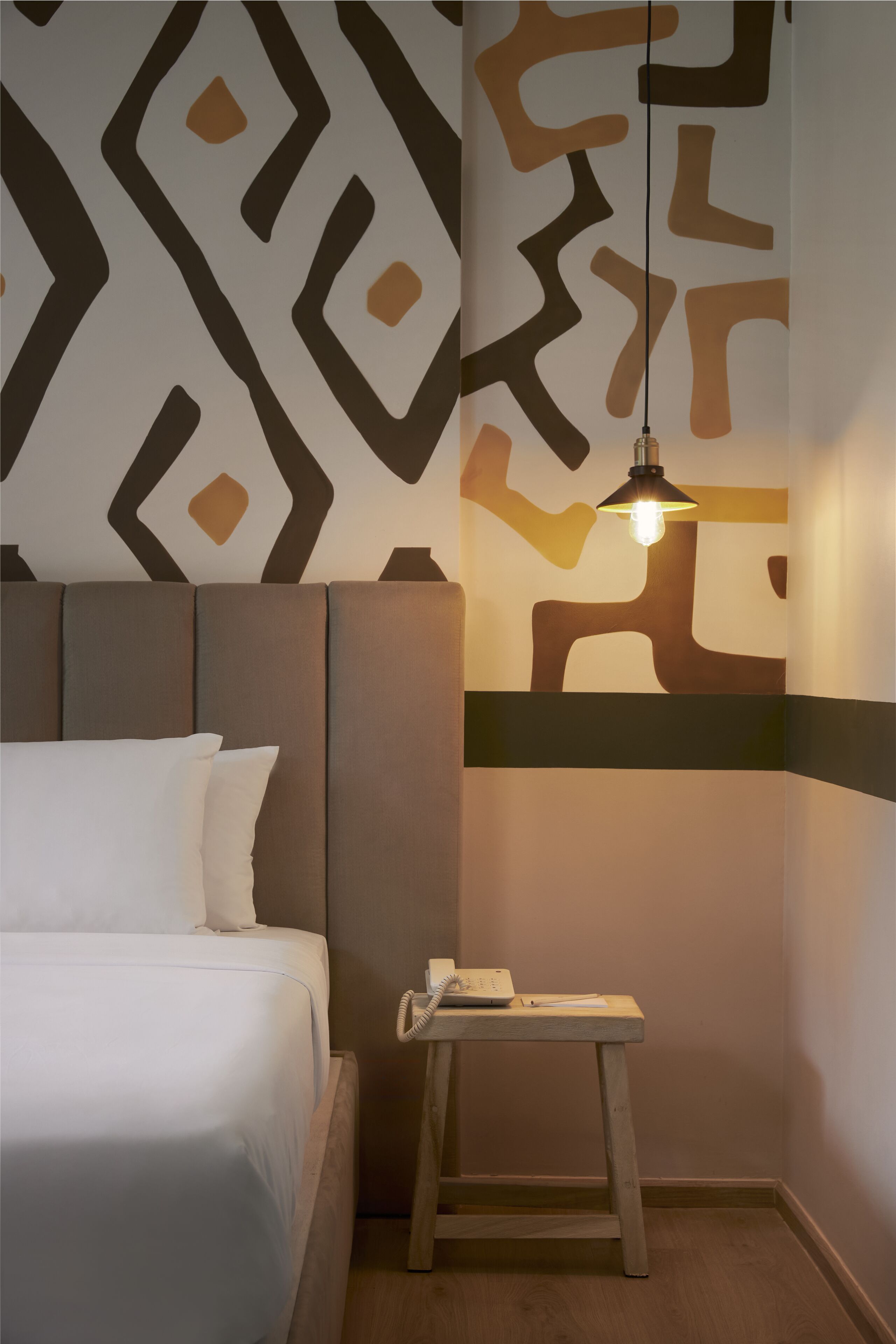 Habitación de hotel con una cama, una mesita de noche con teléfono y una pared con diseño geométrico.