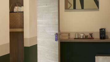 A hotel room with a wooden wardrobe, a kitchenette with a coffee machine, and a wall-mounted artwork.