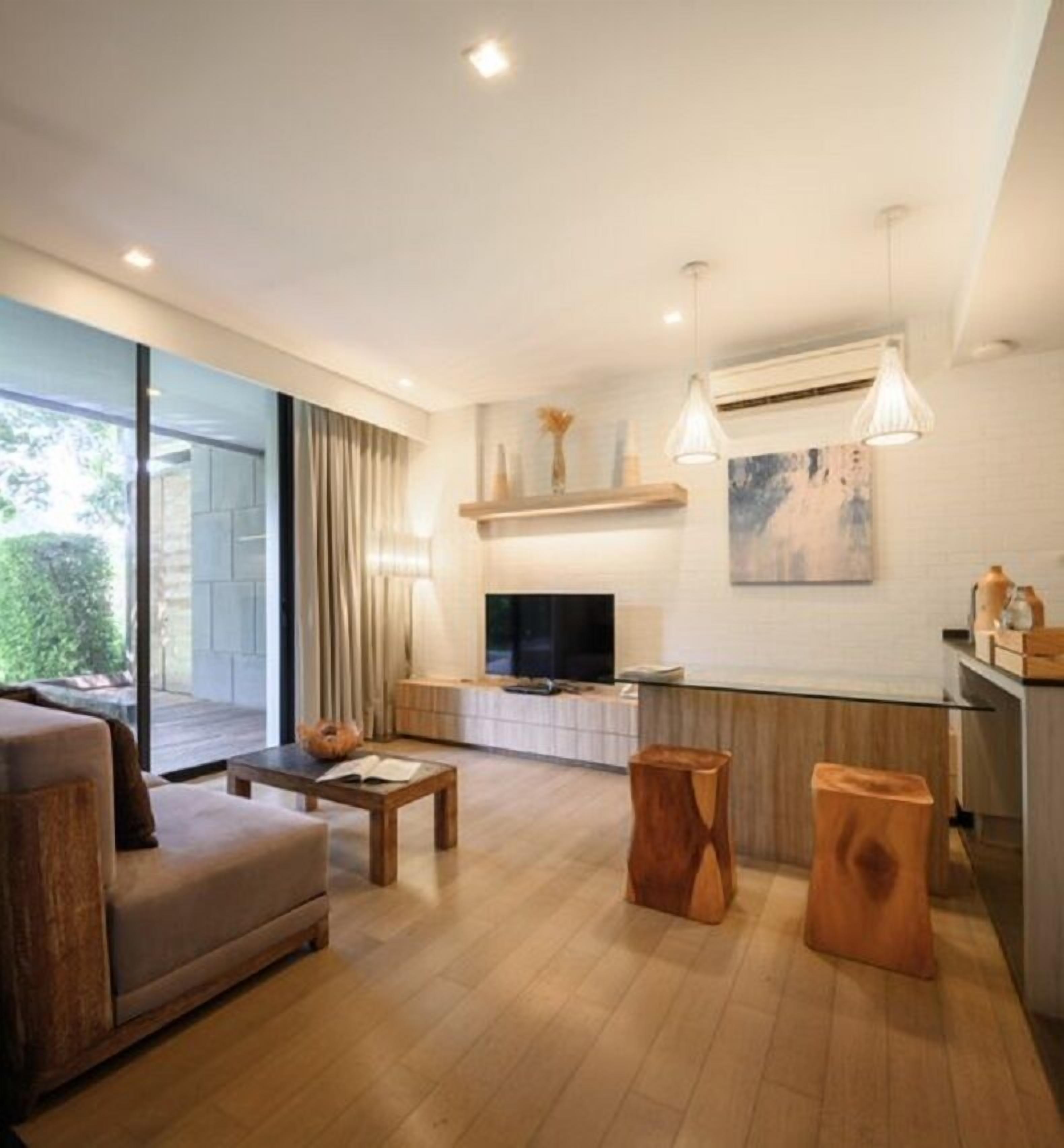 A modern living room with a sofa, coffee table, and wooden stools. There is a TV, a fireplace, and a kitchen area with a countertop.