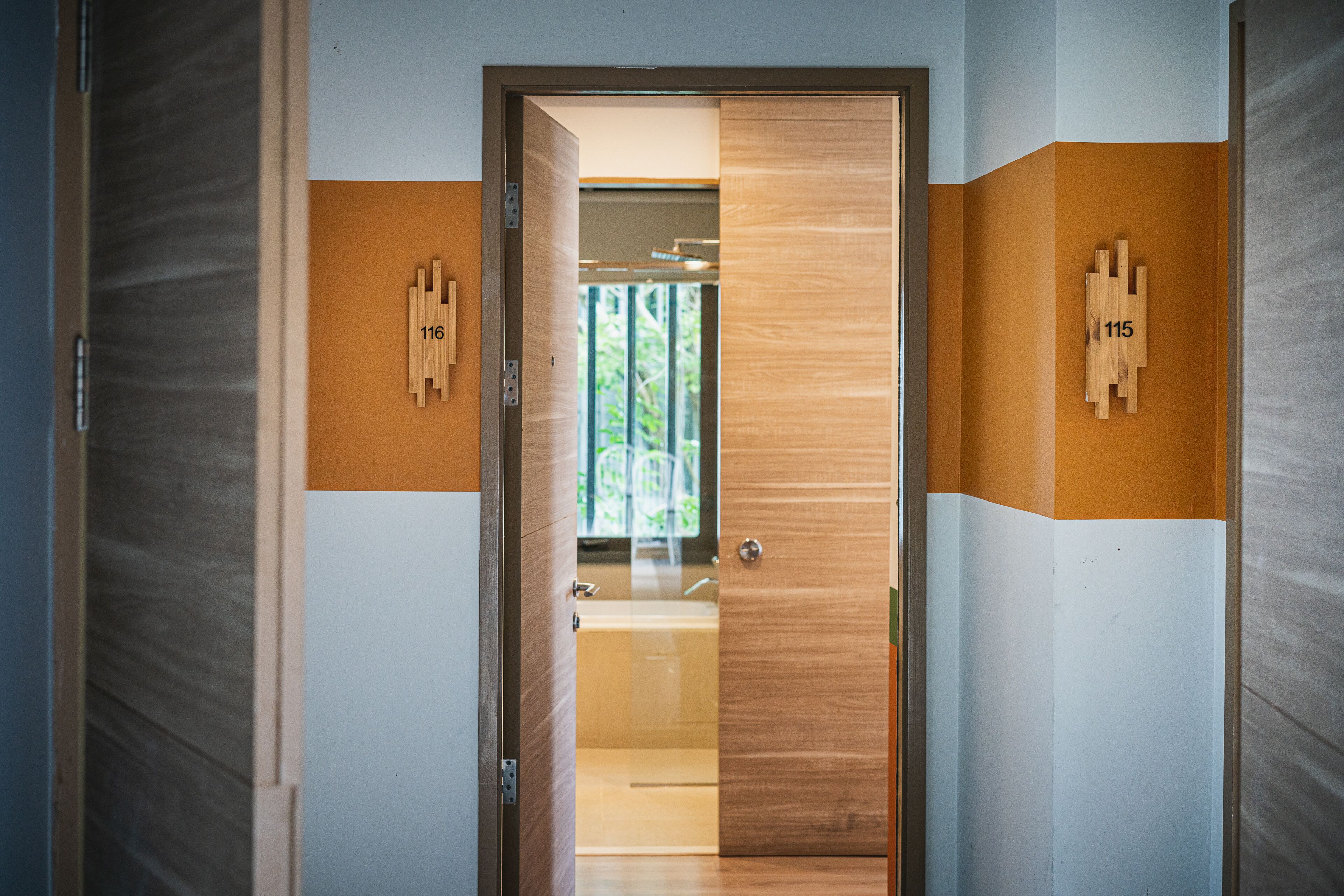 A hallway with a wooden door, numbered plaques, and a view into a room with a bathtub.