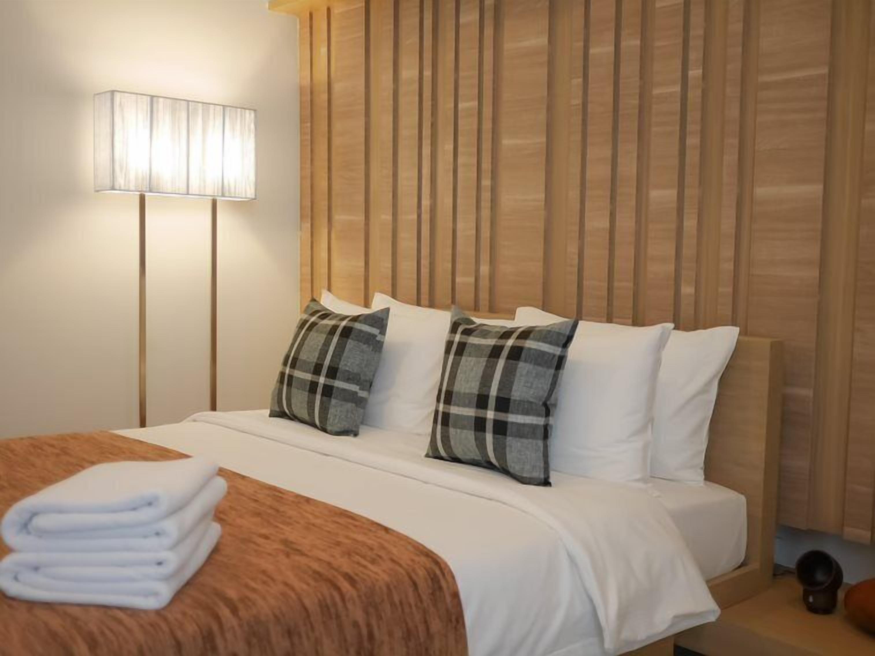 Una habitación de hotel con una cama, una lámpara y un cabecero de madera.