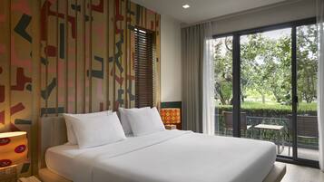 A large bed with white linens, a bedside lamp, and a view of an outdoor patio with chairs and tables.