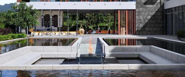 A modern building with a pool area, featuring a central water feature with a fire element, surrounded by seating and greenery. - The Peri Hotel Khao Yai (Pak Chong)