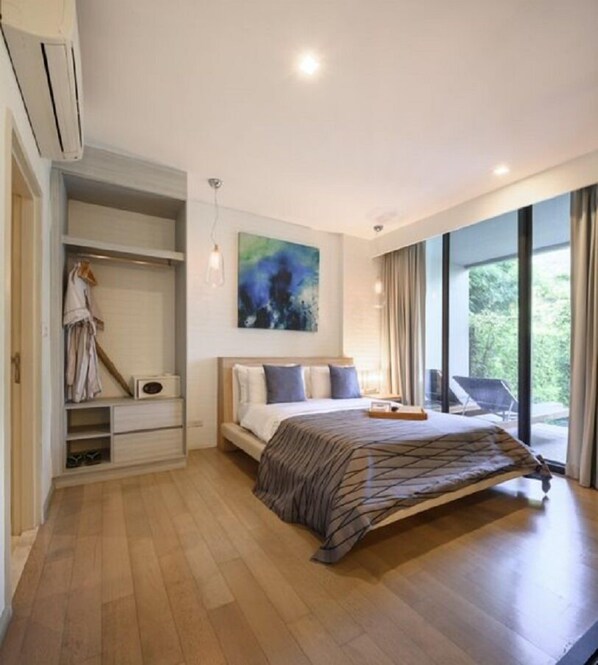 A modern bedroom with a large bed, a walk-in closet, and a view of greenery through the windows.