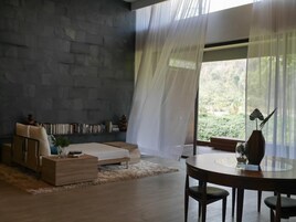 Una sala de estar moderna con una pared de piedra, un sofá, una mesa de centro, una mesa de comedor con sillas y cortinas translúcidas.