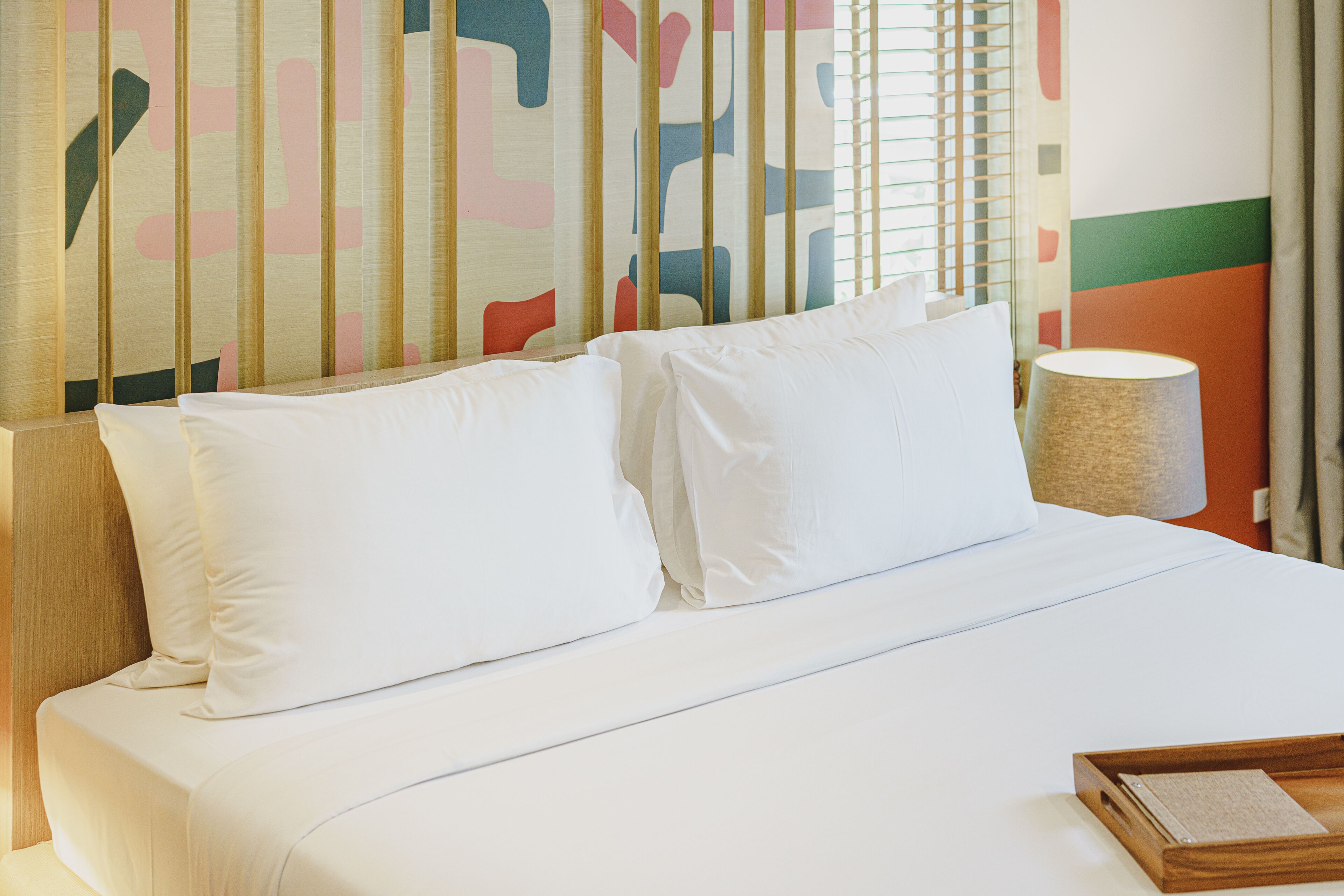 A neatly made bed with white linens, a wooden headboard, and a bedside table with a lamp.