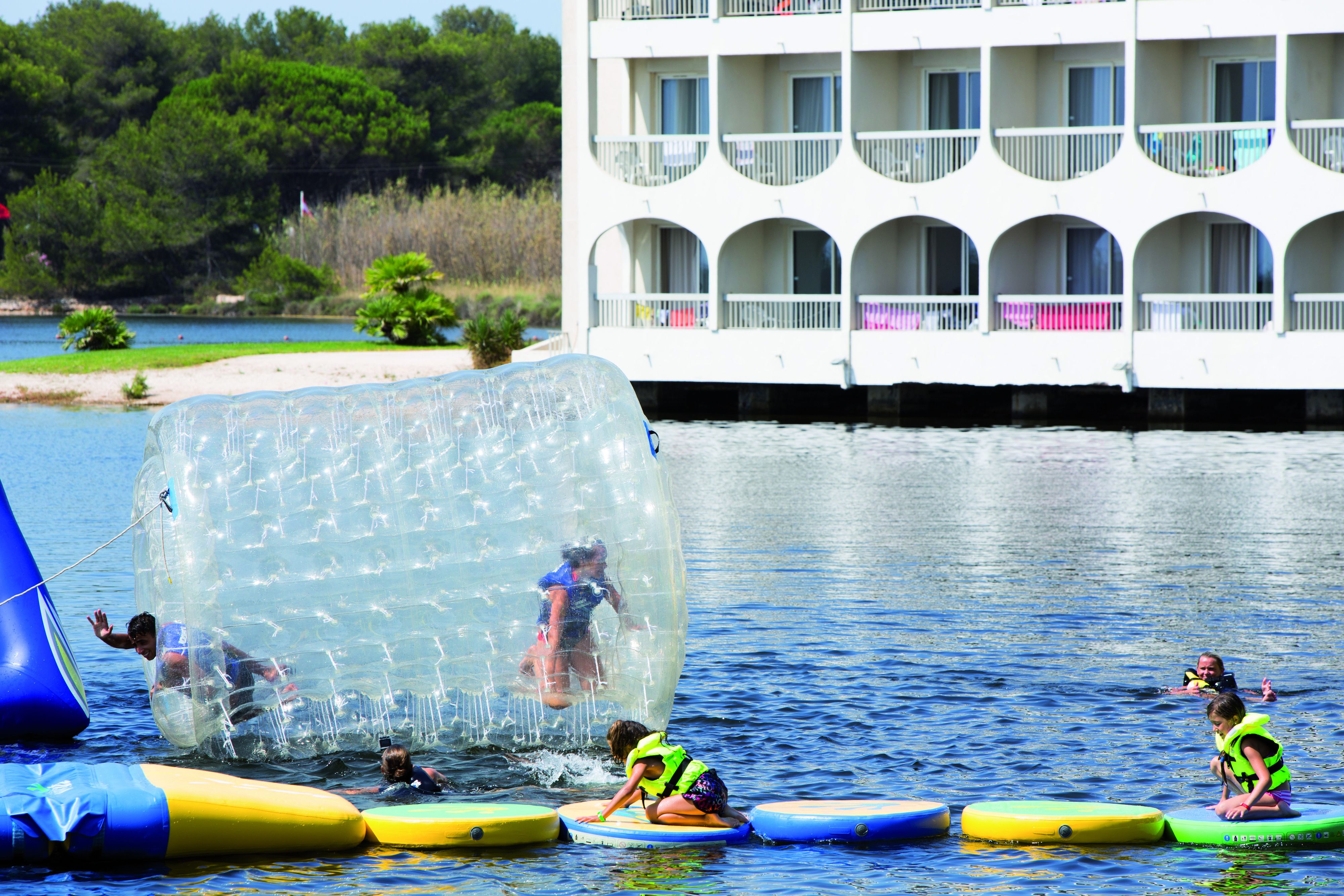 Un parc aquatique avec des structures gonflables et, au fond, un bâtiment doté de balcons.
