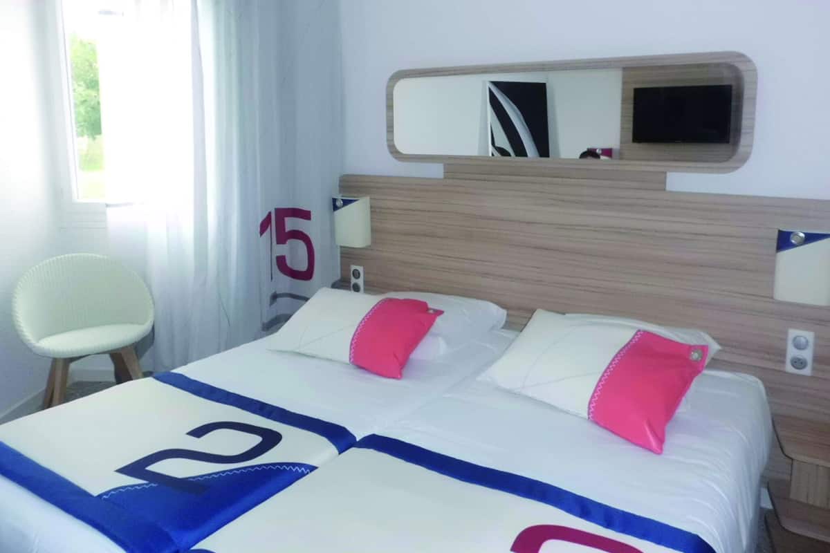 A hotel room with a bed, a chair, a mirror, and a window with curtains.
