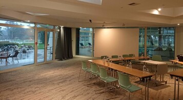 Un salón de conferencias con una gran mesa, sillas verdes y vistas a un patio exterior con sillas y una mesa.
