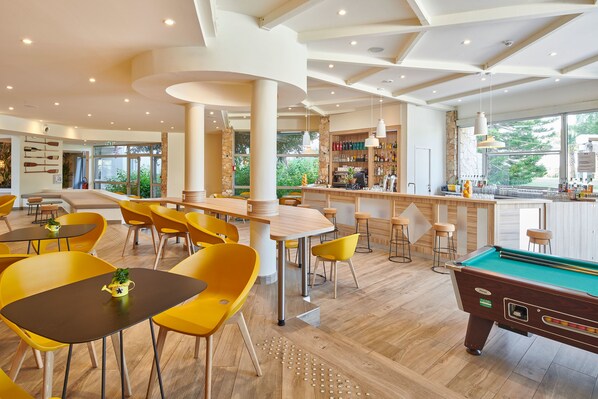 A modern indoor pool area with yellow chairs, a pool table, and a bar area with stools. - Club Vacances Bleues Plein Sud (Hyères)