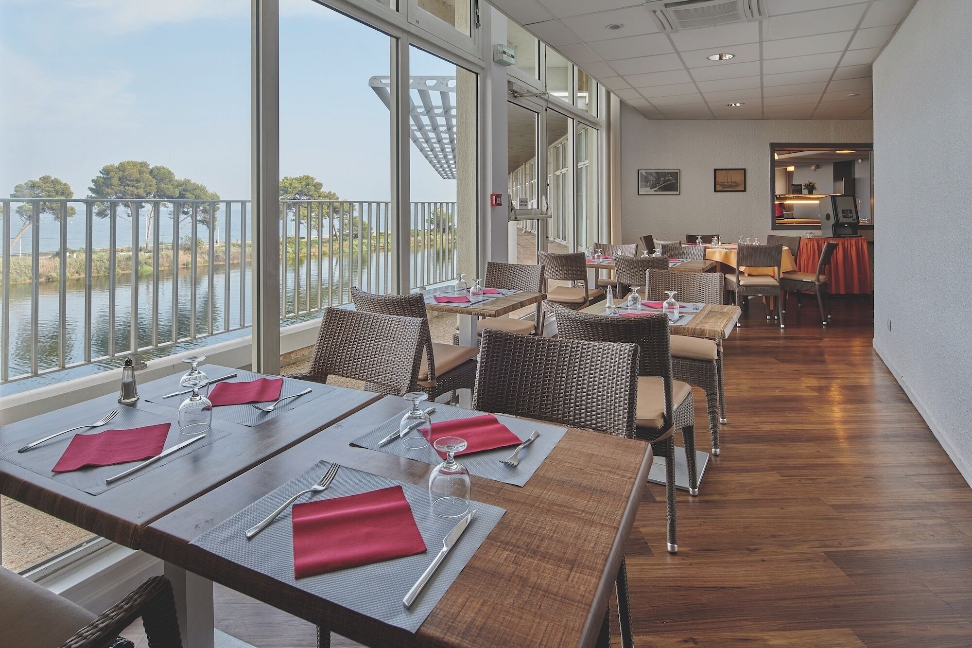 A restaurant with tables set for dining, large windows with a view of the water, and wicker chairs.