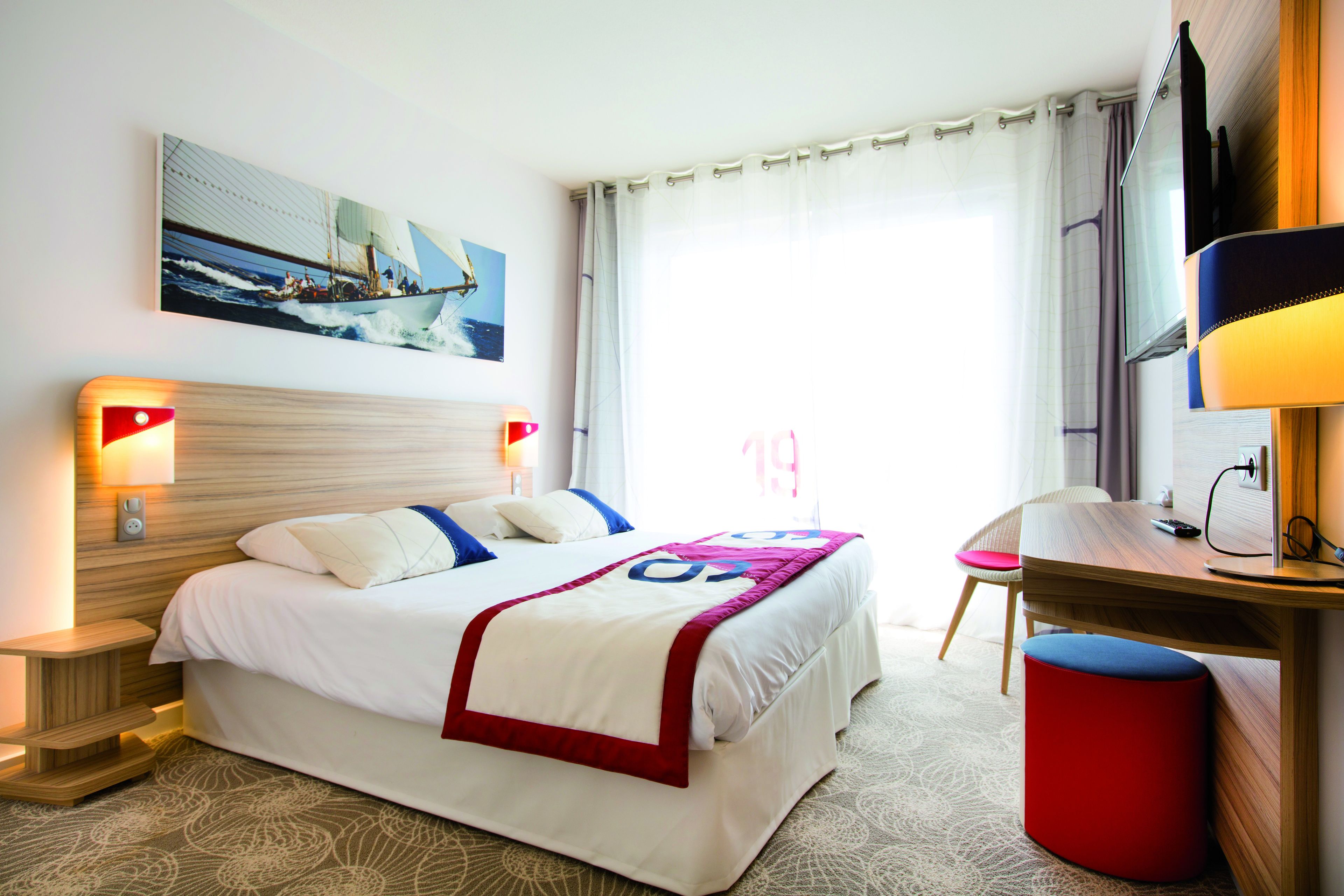 A hotel room with a bed, bedside tables, a desk, a chair, a TV, and a window with curtains.