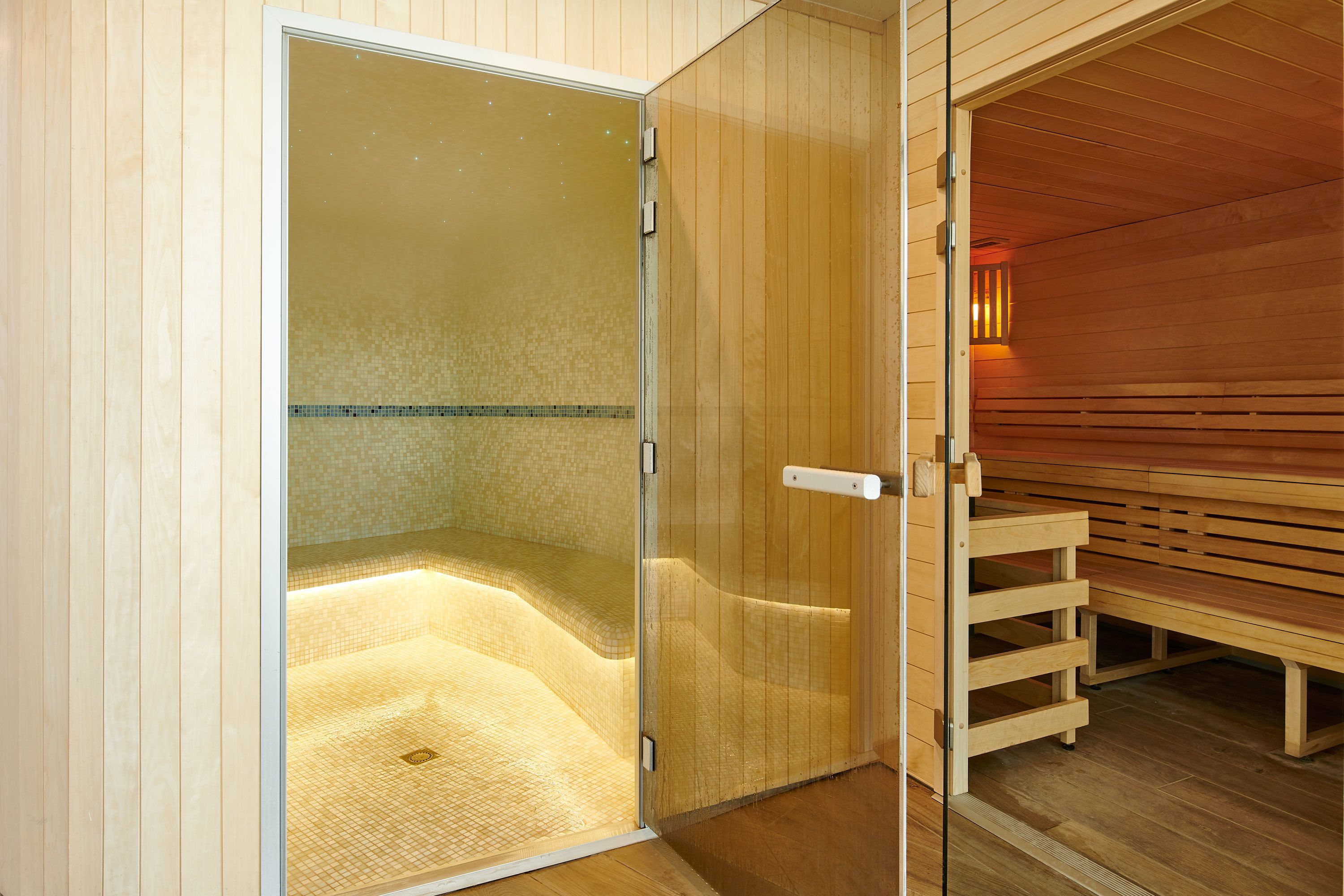 A sauna room with a glass door, wooden benches, and a tiled floor.