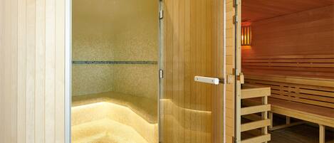 A sauna room with a glass door, wooden benches, and a tiled floor.