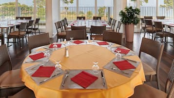 Un comedor con mesas redondas, sillas de mimbre color café y una planta grande en maceta.