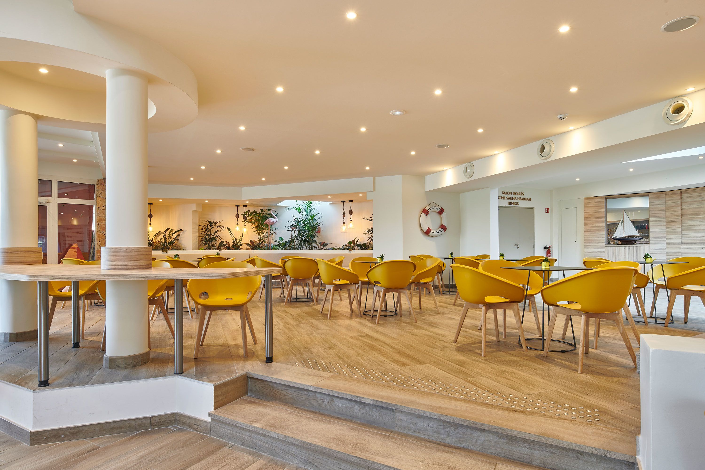 Amplio espacio interior con sillas y mesas amarillas, piso de madera y un diseño moderno de techo.