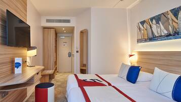 A hotel room with a bed, bedside table, TV, and a painting of sailboats.